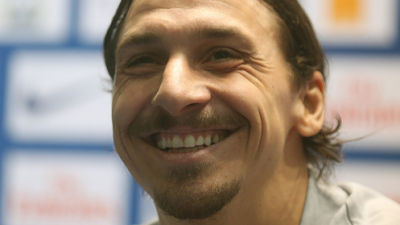 Zlatan ler stort. Han har håret i en hästsvans och har en grå tröja på sig.