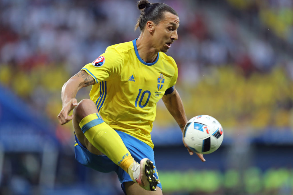 Zlatan plockar ner en fotboll från luften med ena foten. Han har gula och blå landslagskläder på sig och på tröjan syns siffran 10.