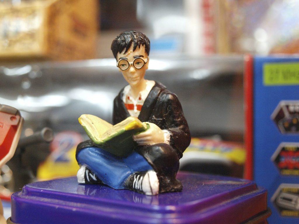 En liten leksaksfigur föreställer Harry Potter som sitter ner med en bok i famnen.