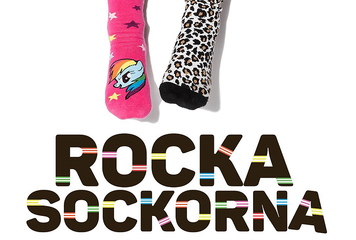 Två fötter sticker in i bilden uppifrån. Ena foten har en rosa strumpa med en enhörning. Den andra foten har en leopardfärgad strumpa. Under fötterna står det med stora bokstäver "Rocka sockorna".
