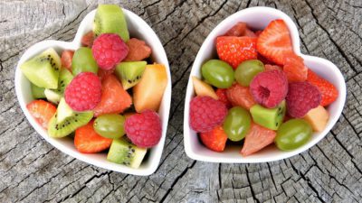 Två skålar med frukt. Skålarna är hjärtformade. Det är vindruvor, jordgubbar, hallon, kiwi och apelsin i skålarna.