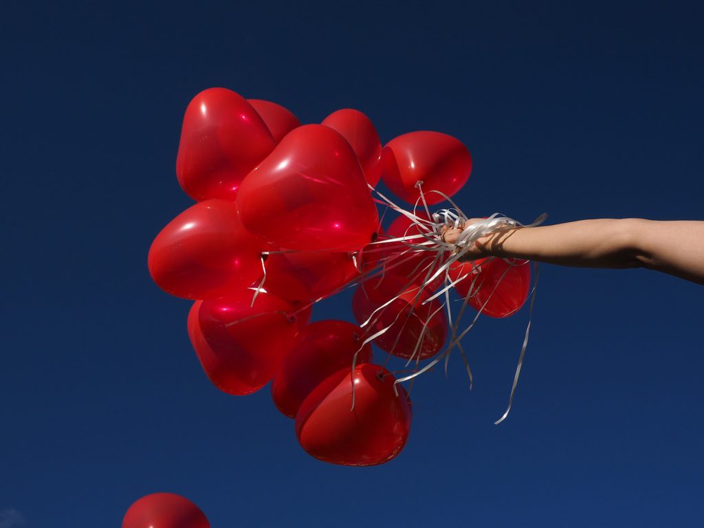 Bild på en hand som håller i ett tjugotal ballonger formade som hjärtan.
